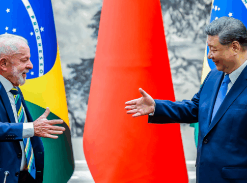 Dois líderes políticos, um do Brasil e outro da China, sorriem e estendem as mãos para um cumprimento diante das bandeiras de seus países.