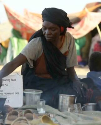 Uma mulher sudanesa deslocada prepara chá enquanto outras pessoas se reúnem e sentam em tendas improvisadas após fugirem da cidade de Al-Fashir, em Darfur, em Tawila, Sudão, em 29 de outubro de 2025