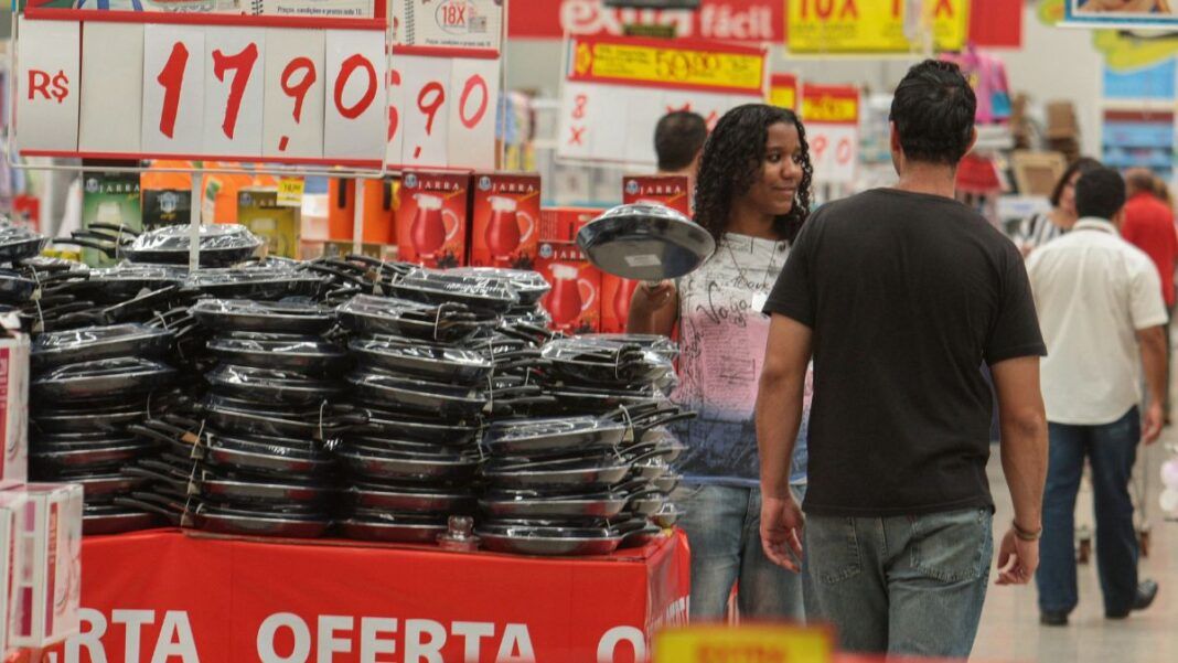 Pessoas circulam dentro de mercado entre placas de preços
