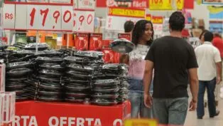 Pessoas circulam dentro de mercado entre placas de preços