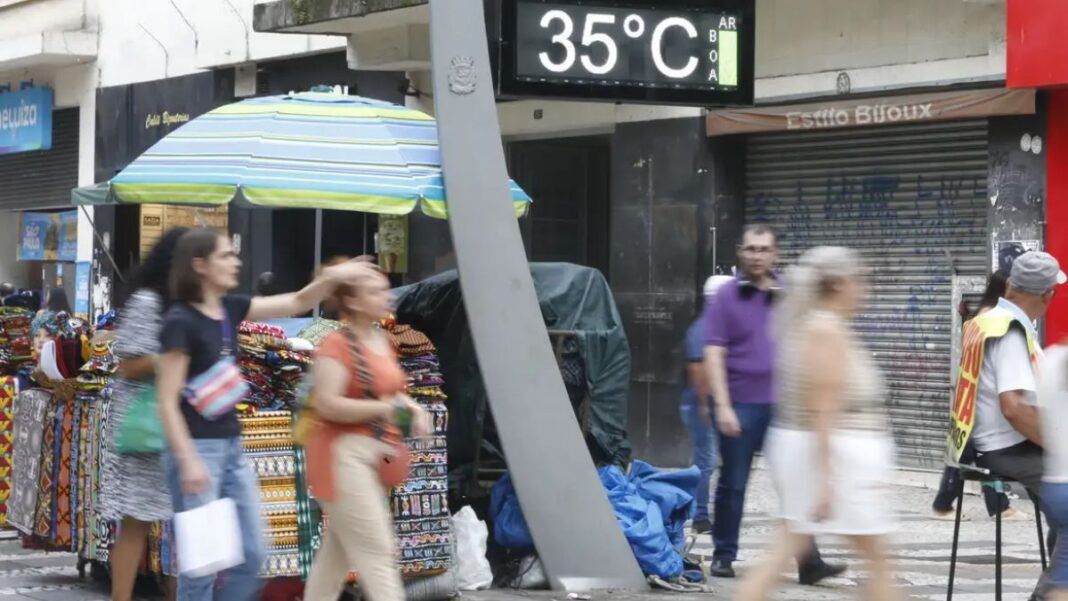 Imagem mostra um termômetro de rua mostrando a temperatura em 35º C com pessoas caminhando ao redor