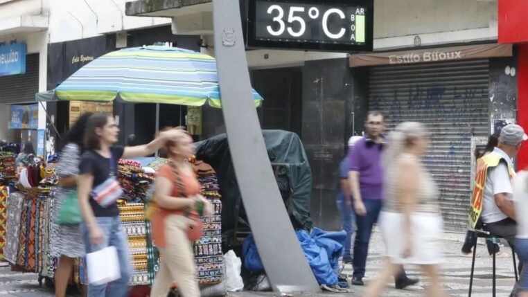 Imagem mostra um termômetro de rua mostrando a temperatura em 35º C com pessoas caminhando ao redor