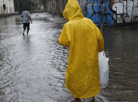 Homem caminha em rua alagada devido a chuva forte