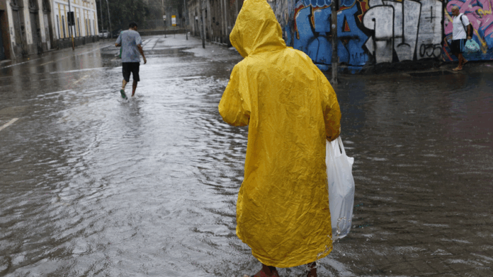 Homem caminha em rua alagada devido a chuva forte