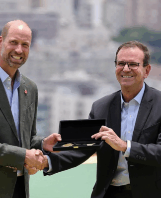 Dois homens de terno trocam um aperto de mão enquanto um deles segura uma caixa aberta com uma chave dourada em seu interior, com prédios desfocados ao fundo.
