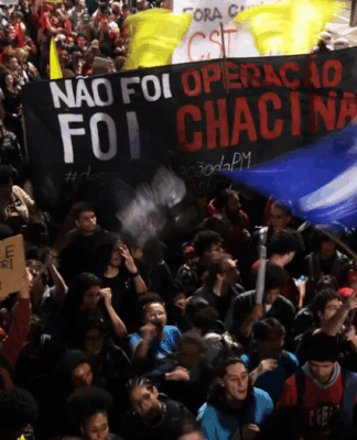 Multidão participa de manifestação à noite segurando faixas e cartazes. Um dos principais cartazes diz “Não foi operação, foi chacina”, e outro, “A juventude quer viver! Parem de nos matar!”. Bandeiras coloridas são erguidas entre os manifestantes.