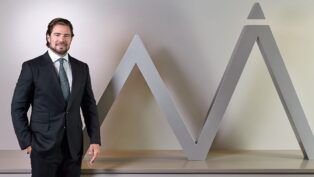 Daniel Vorcaro figura à frente do logo do seu banco vestido de terno e gravata