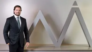 Daniel Vorcaro figura à frente do logo do seu banco vestido de terno e gravata