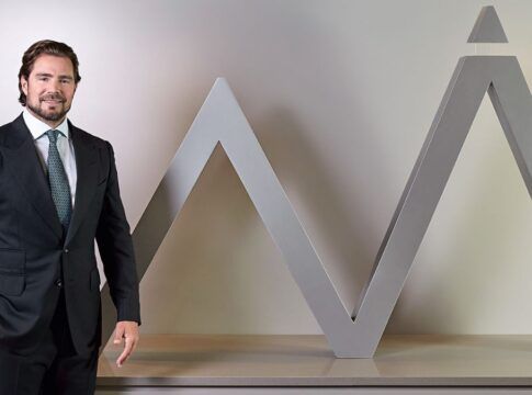 Daniel Vorcaro figura à frente do logo do seu banco vestido de terno e gravata