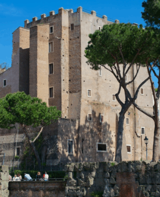 Vista diurna da Torre dei Conti em Roma, uma estrutura medieval de tijolos cercada por árvores altas e edifícios históricos sob um céu azul claro.