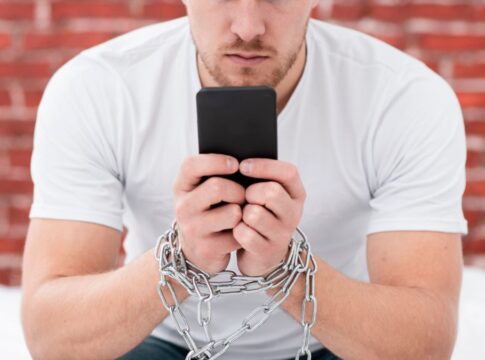 Homem sentado segurando celular com correntes nas mãos