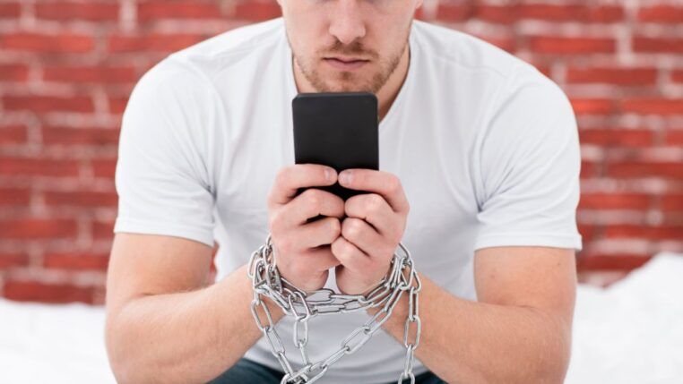 Homem sentado segurando celular com correntes nas mãos