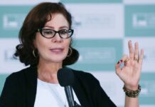 Carla Zambelli, na época em que era parlamentar, vestindo roupa formal e gesticulando com o sinal de 