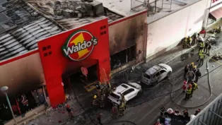 Imagem aérea mostra fachada queimada de uma loja Waldo’s, no México, após um incêndio. Bombeiros e equipes de resgate trabalham no local, ao lado de carros carbonizados e escombros espalhados pela rua.