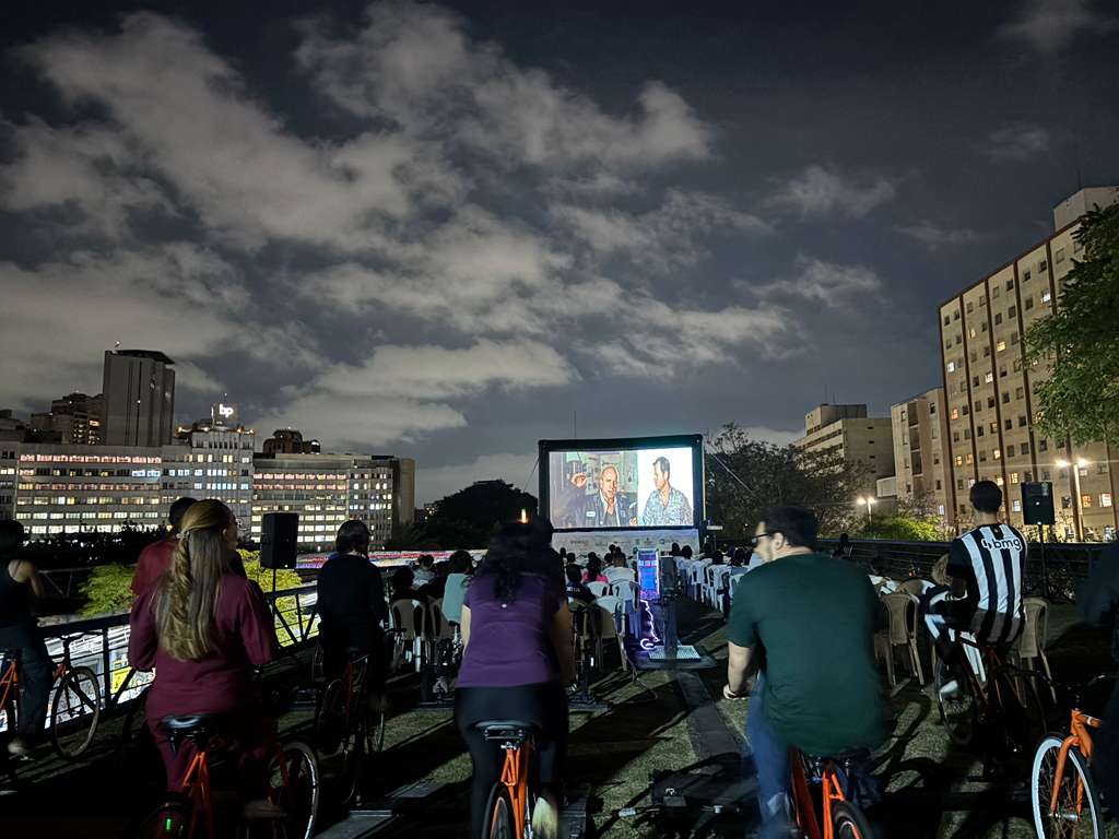 Pessoas pedalando bicicletas enquanto assistem um filme em um telão