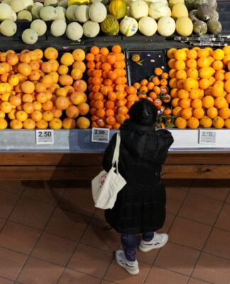 Bancada com frutas e uma mulher agachada escolhendo um produto.