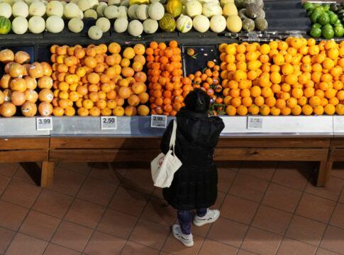 Bancada com frutas e uma mulher agachada escolhendo um produto.