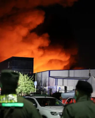 Policiais e bombeiros observam chamas de incêndio em edifício de parque industrial em Ezeiza, na Argentina