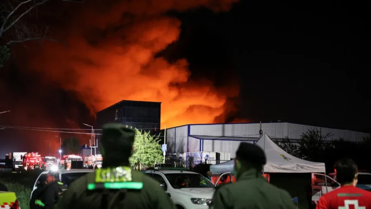 Policiais e bombeiros observam chamas de incêndio em edifício de parque industrial em Ezeiza, na Argentina