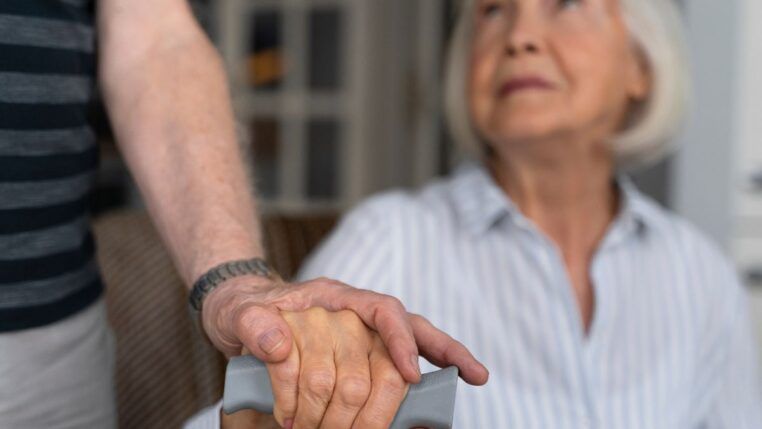 Em imagem ilustrativa, idosa recebe auxílio de um cuidador.