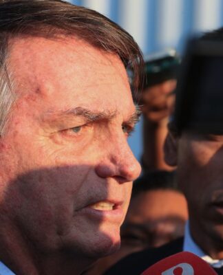 Esta é um close-up lateral do ex-presidente brasileiro Jair Bolsonaro em um ambiente externo, provavelmente falando ou respondendo a jornalistas.