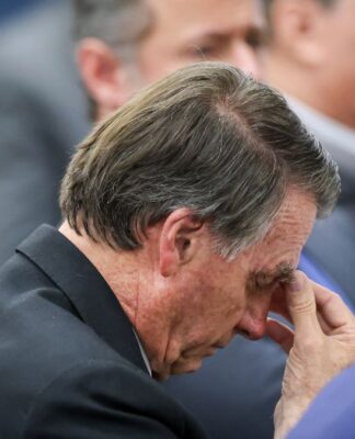 Imagem mostra o ex-presidente Jair Bolsonaro pensativo com a cabeça baixa e mão sobre a testa.