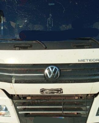 Imagem mostra caminhão branco parado no meio de uma rodovia. O para-brisa do veículo tem uma avaria, com um buraco no canto superior esquerdo