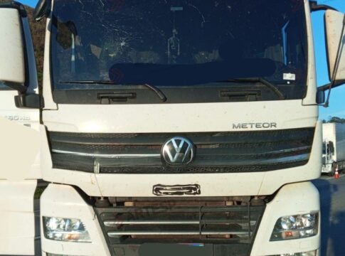 Imagem mostra caminhão branco parado no meio de uma rodovia. O para-brisa do veículo tem uma avaria, com um buraco no canto superior esquerdo