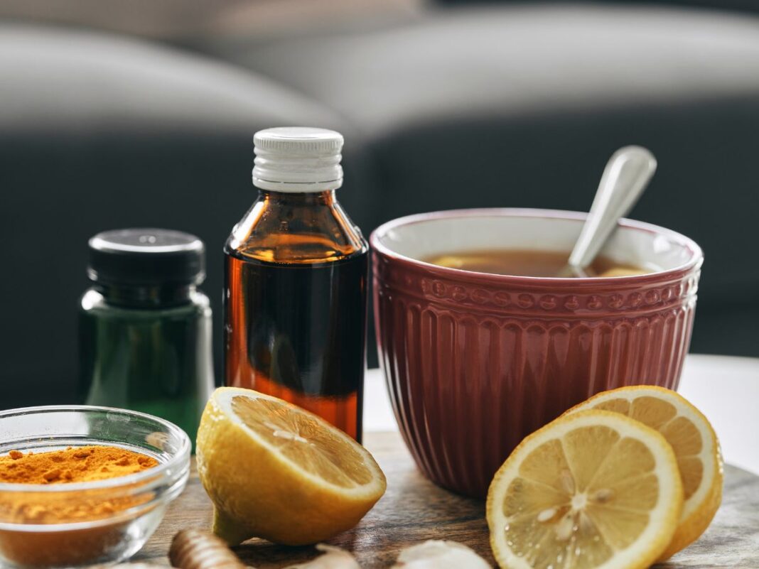 Em imagem ilustrativa, alguns fracos de medicamentos, chás e limões cortados estão sob a mesa