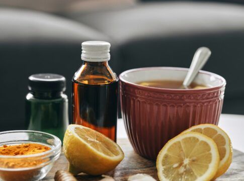 Em imagem ilustrativa, alguns fracos de medicamentos, chás e limões cortados estão sob a mesa