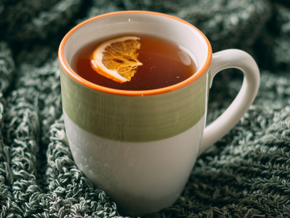 Na foto há uma xícara branca com detalhe em verde. Nela há um líquido com um laranja.