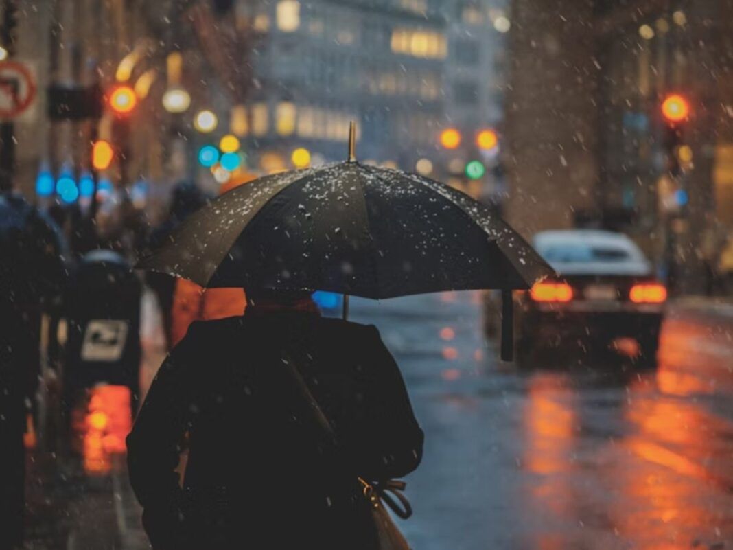 A imagem mostra uma pessoa de costas usando um guarda-chuva na rua enquanto chove muito