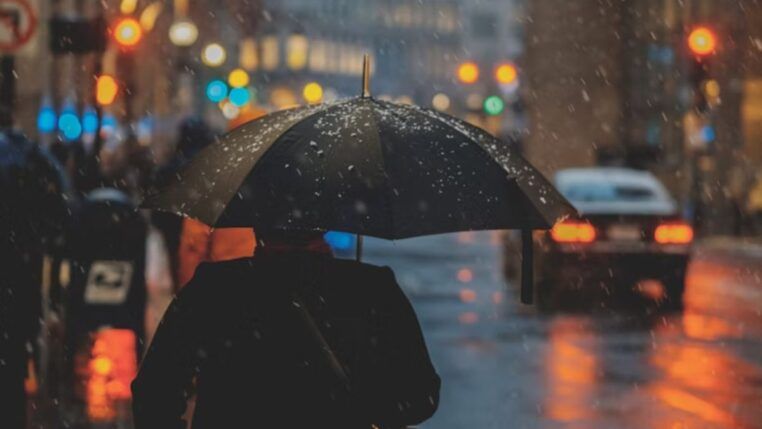 A imagem mostra uma pessoa de costas usando um guarda-chuva na rua enquanto chove muito