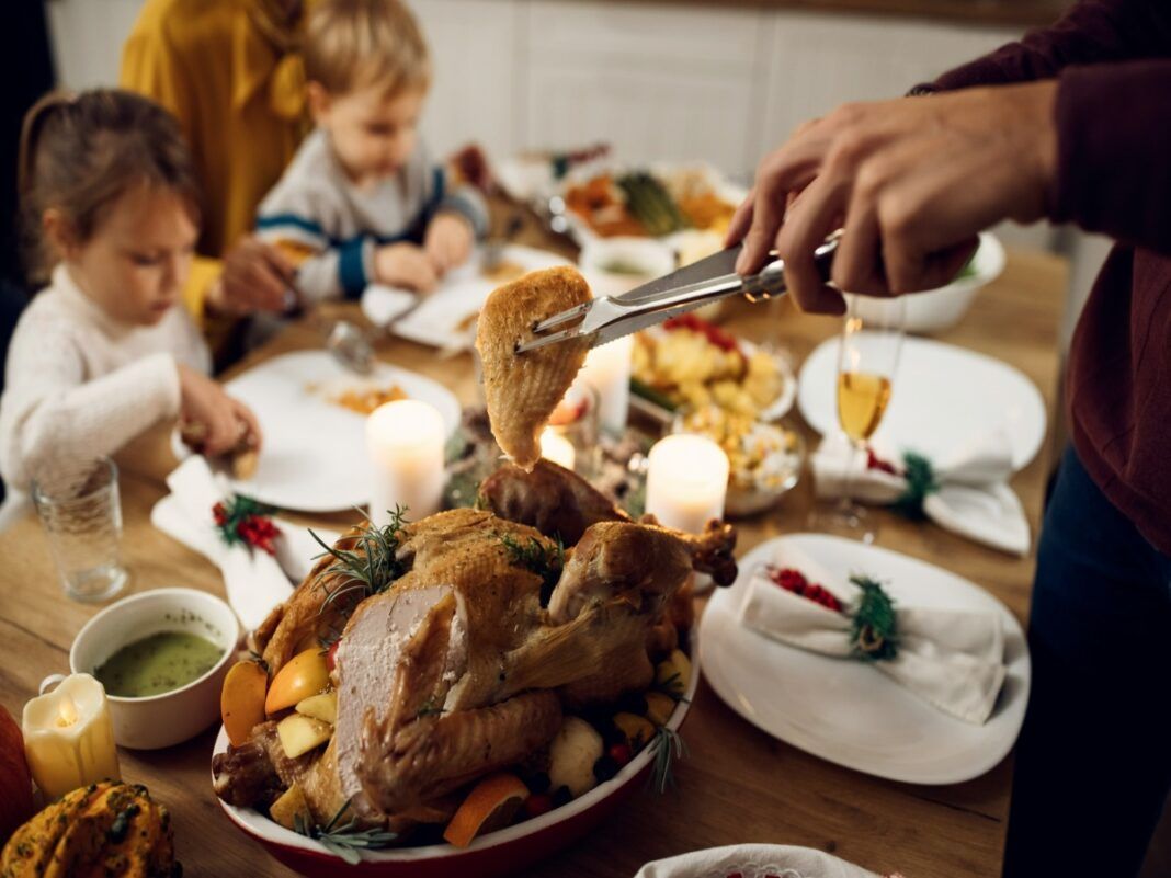 Close de a mão de um homem cortando um pedaço de frango na ceia de natal