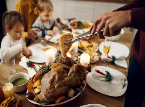 Close de a mão de um homem cortando um pedaço de frango na ceia de natal