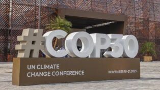 Imagem mostra o letreiro da COP30, em Belém, com fonte branca sobre uma bancada marrom.