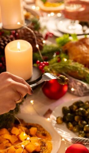 Na foto há uma mesa de jantar em que há muitos pratos, velas e pessoas comendo.