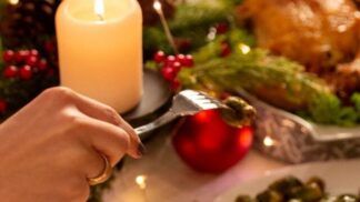 Na foto há uma mesa de jantar em que há muitos pratos, velas e pessoas comendo.