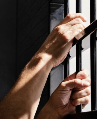 Imagem mostra as mãos de um detento segurando as grades da prisão