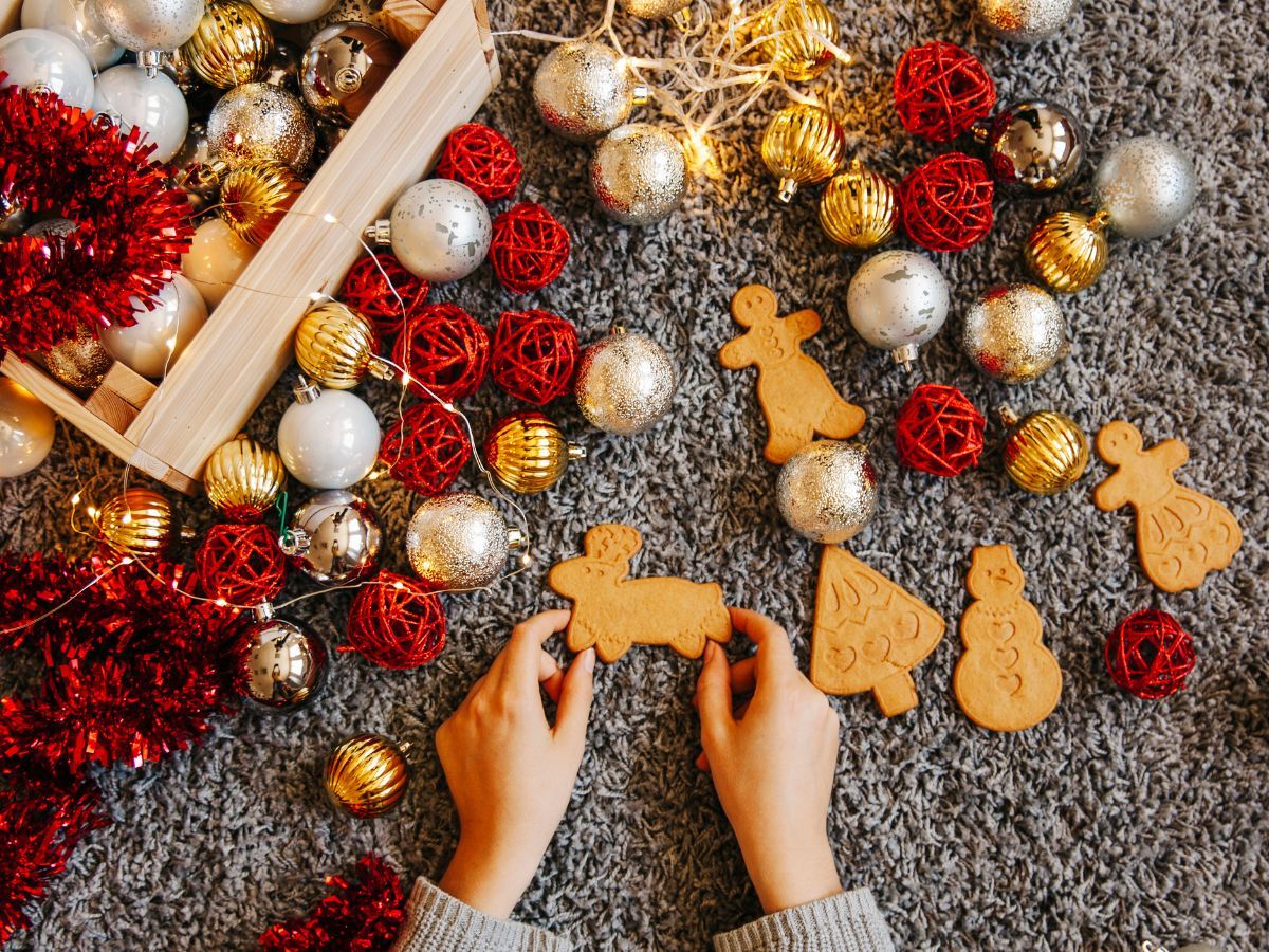 imagem mostra uma mão feminina mexendo em decorações de Natal vermelhas, brancas e douradas