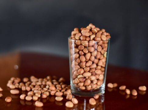 E imagem ilustrativa, há um copo estilo americano com feijões dentro e grãos caídos a mesa.