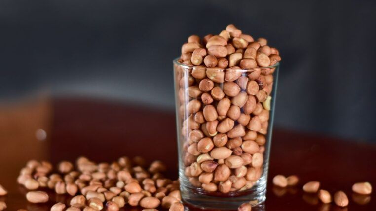 E imagem ilustrativa, há um copo estilo americano com feijões dentro e grãos caídos a mesa.