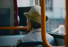 Um homem de costas sentado num ônibus, ele usa chapéu