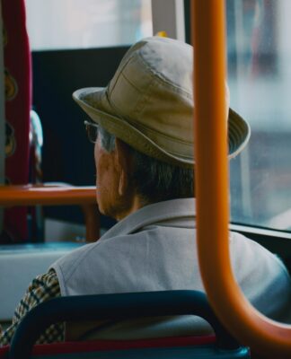 Um homem de costas sentado num ônibus, ele usa chapéu