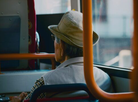 Um homem de costas sentado num ônibus, ele usa chapéu