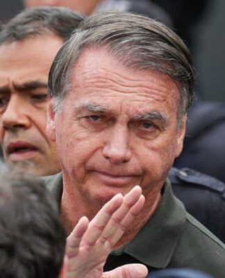 Imagem mostra o ex-presidente Jair Bolsonaro em primeiro plano. Atrás dele, aparece metade do rosto de um homem.