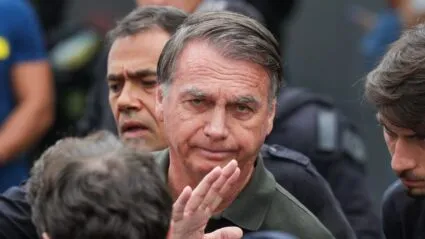 Imagem mostra o ex-presidente Jair Bolsonaro em primeiro plano. Atrás dele, aparece metade do rosto de um homem.