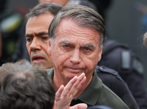 Imagem mostra o ex-presidente Jair Bolsonaro em primeiro plano. Atrás dele, aparece metade do rosto de um homem.