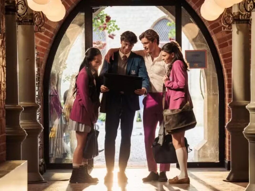 Na foto estão 4 jovens com uniformes que possuem cores cinza r osa. Eles estão em um corredor e olhando para um tablet.