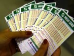 Pessoa segura em suas mãos cartões de apostas da Mega Sena